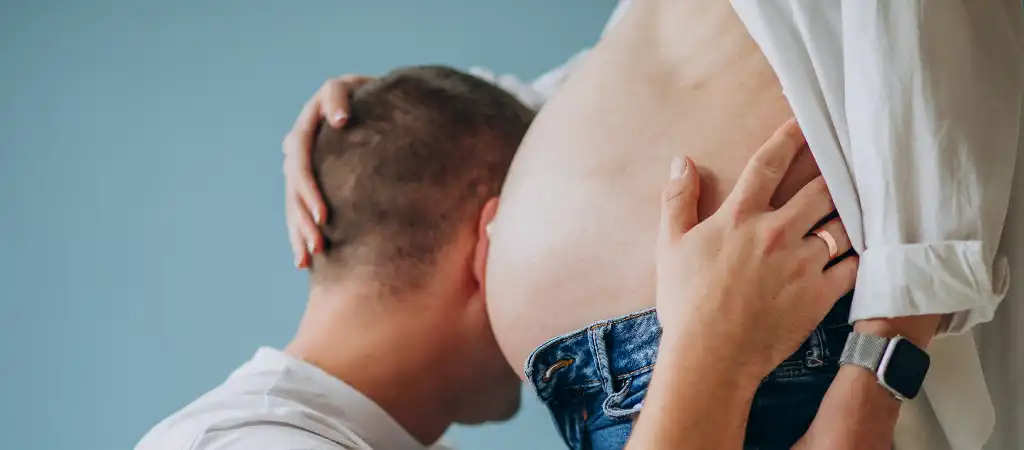 Online szülés kalkulátor, várandós nő hasát hallgató férje.
